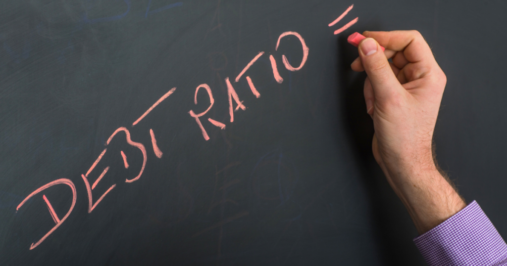 Hand writing "DEBT RATIO" in chalk on a blackboard.