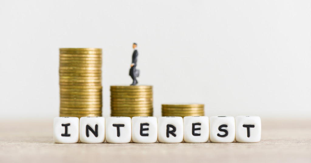 Miniature person on stacked coins beside "INTEREST" blocks.