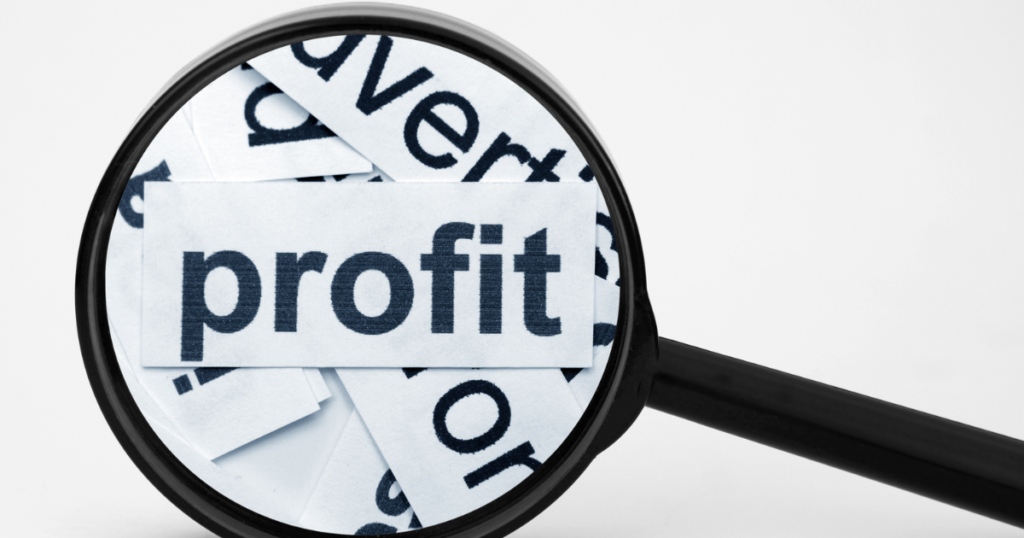 Magnifying glass focusing on the word "profit" among other cut-out newspaper words.